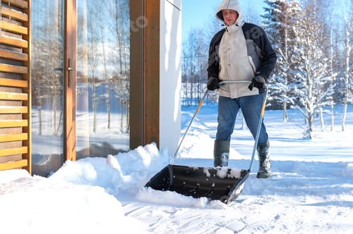 Preview: A man in winter clothes with a snow shovel cleaning the snow from the terrace of the house