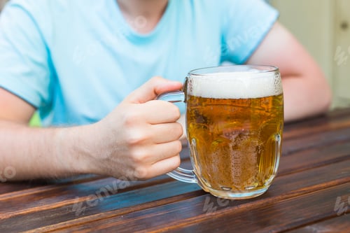 Preview: Hand holding a glass of beer on wooden table