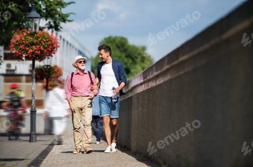 Preview: Young man and blind senior with white cane walking on pavement in city