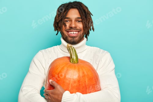 Preview: Portrait of happy smiling guy has happy mood, carries big orange pumpkin, ready to cook vegetable di