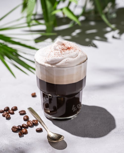 Preview: Iced coffee in a glass with foam on a light background with palm leaves, coffee beans