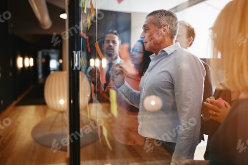 Preview: Manager reading sticky notes with his team in an office