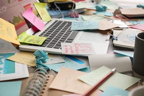 Preview: Laptop, notes and office stationery in mess on desk. Overwhelmed with work