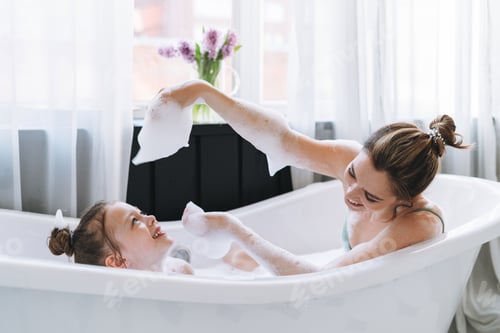 Preview: Young mother with little daughter having fun in bath with foam at home