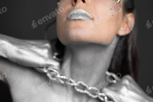 Preview: Beautiful woman with silver paint on her skin and hair breaks the chain around her neck