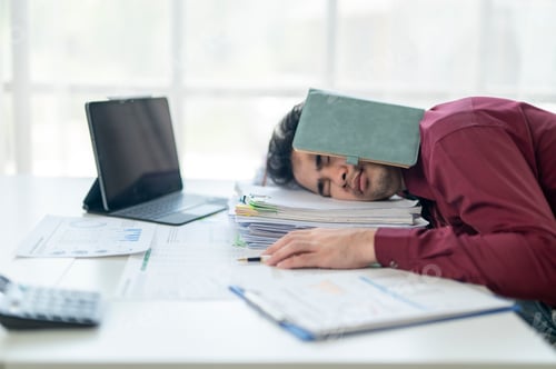 Preview: A man is sleeping on his desk with a book on his head