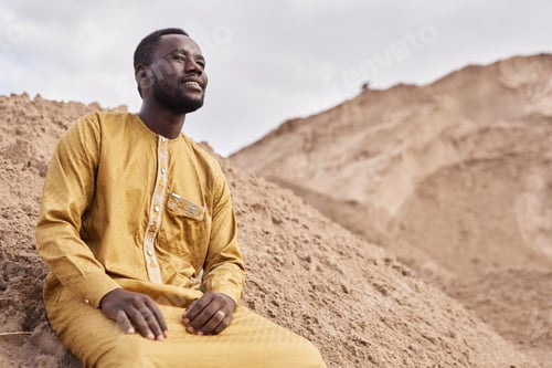 Preview: Smiling African American Man in Traditional Kaftan Looking at View in Desert