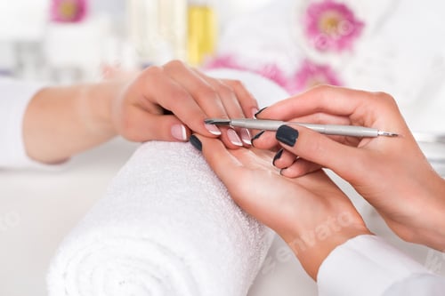 Preview: close up image of woman receiving manicure by beautician with cuticle pusher at table with flowers