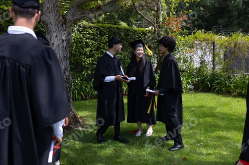 Preview: Celebrating graduation, diverse students in caps and gowns holding diplomas outdoors