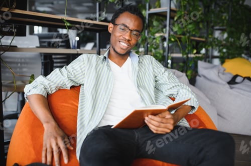 Preview: Smiling african american student reading a book in university library