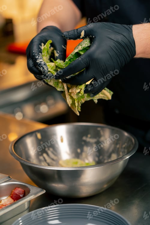 Preview: close-up in a professional kitchen the chef mixes lettuce leaves with sauce with his hands