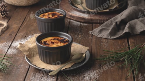 Preview: Two creamy, caramelized desserts in dark ramekins sit on a rustic wooden table