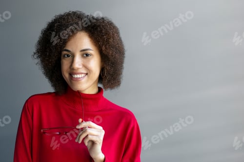 Preview: Confident elegant African American pretty woman, holding eyeglasses, smiles cutely looking at camera