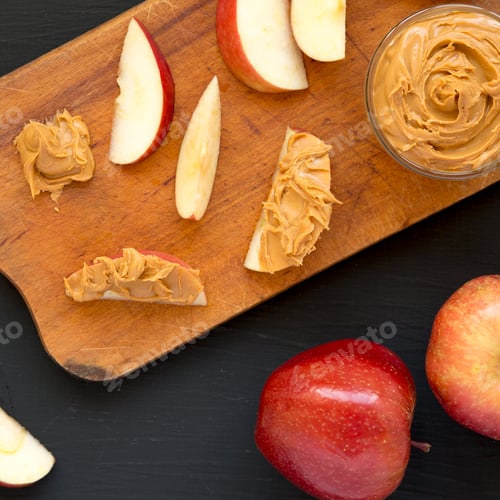 Preview: Raw Red Apples and Peanut Butter on a rustic wooden board on a black surface, top view.