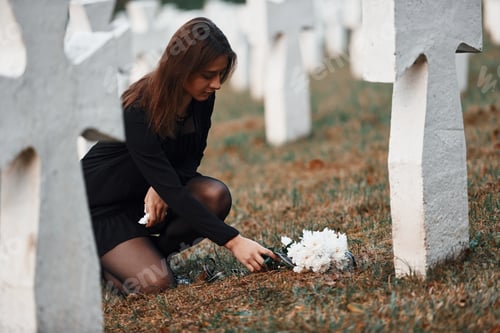 Preview: Young woman in black clothes visiting cemetery with many white crosses