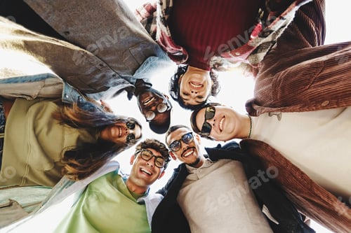 Preview: Multiethnic group of young friends joining heads in circle watching down to the camera