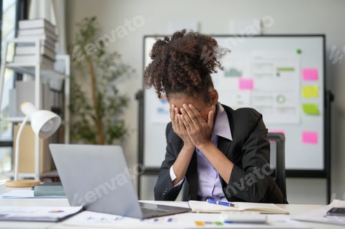 Preview: Stressed businesswoman covering her face with hands at office desk