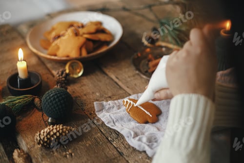 Preview: Hands decorating gingerbread cookie christmas tree with frosting on rustic table with napkin, decor