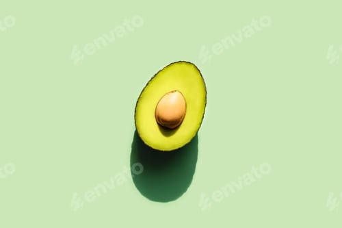 Preview: Avocado cut in half in sunlight. Neo mint green background. Front view.