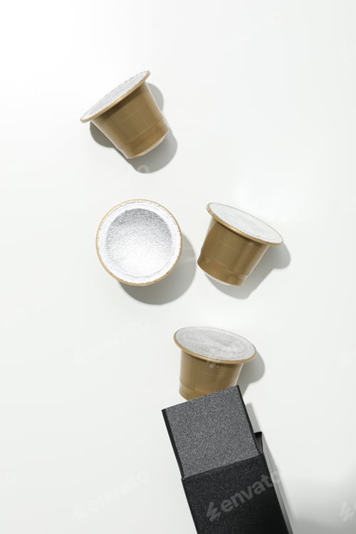 Preview: Golden coffee capsules on black box on white background, top view