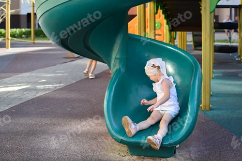 Preview: A two-year-old girl slides down a children's slide. Modern playground. Active recreation in the city