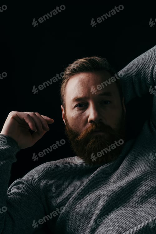 Preview: Portrait of bearded man in grey long sleeve posing in light isolated on black