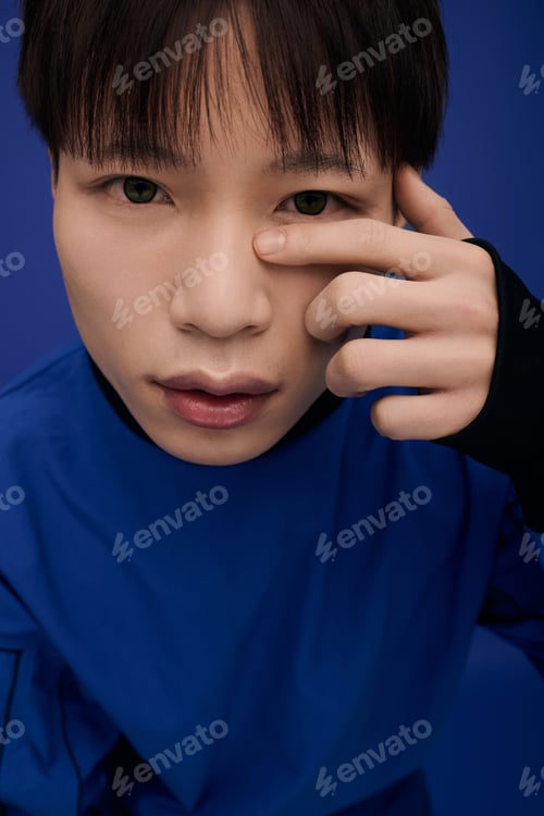 Preview: Young handsome Asian man thoughtfully posing against a deep blue background with an artistic flair