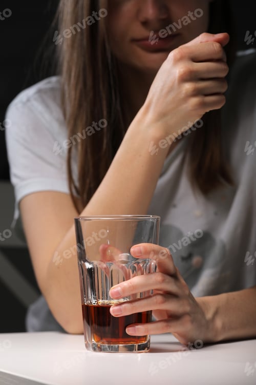 Preview: Close up of woman sitting and holds glass with whiskey or cognac having alcohol addiction, depressed