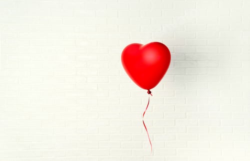 Preview: Red ballon with heart shape hangs aganst white wall