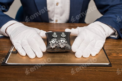 Preview: Cropped view of jewelry appraiser holding jewelry earnings on jewelry pillow near board on table