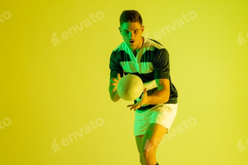 Preview: Caucasian male rugby player catching rugby ball over yellow lighting