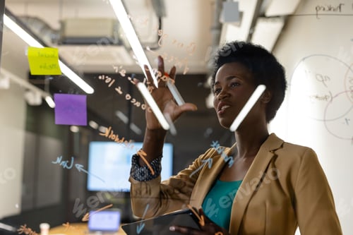 Preview: African American woman marking notes on glass wall with orange marker in office, copy space