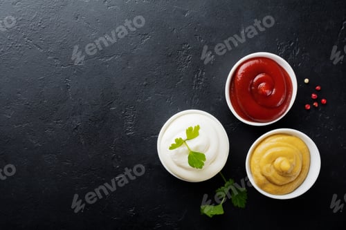 Preview: Set of three sauces - mayonnaise, mustard and ketchup in white ceramic bowls on black stone or concr