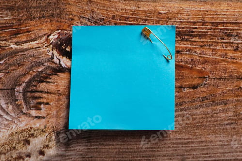 Preview: Light blue paper note attached with safety pin on wooden table, top view. Space for text