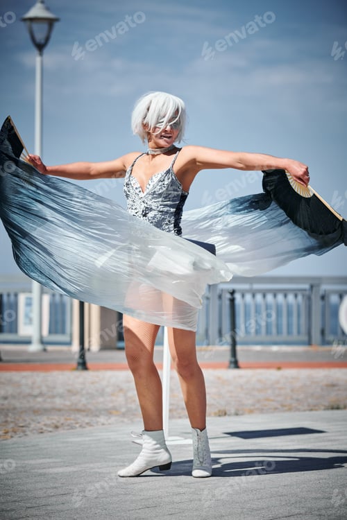 Preview: Young sexy girl in silver micro skirt dancing with performance fan waving gracefully, outdoor dance