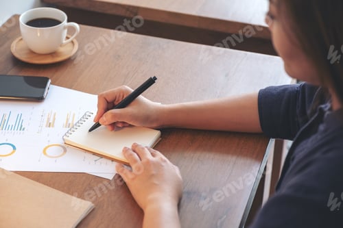 Preview: A businesswoman writing on notebook and working on business data and document on the table in office