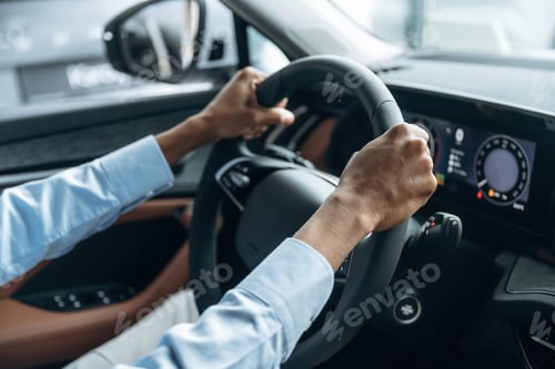 Preview: Hands are on the steering wheel. Man in shirt is in the modern car