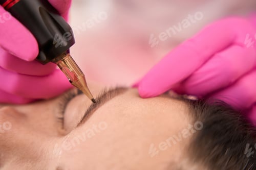 Preview: Master in pink gloves makes a tattoo of womans eyebrows