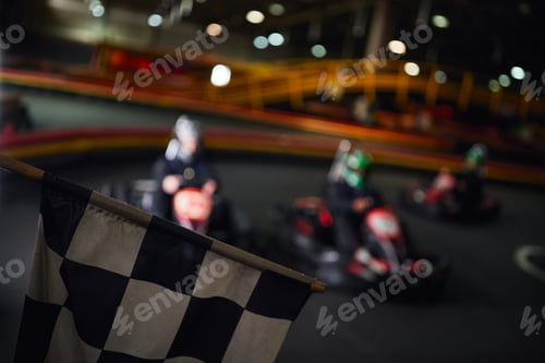 Preview: checkered black and white racing flag with drivers on blurred backdrop, go kart concept