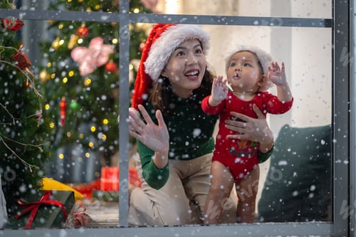 Preview: Asian baby and woman watching falling snow in house by window. Outside the house, it is snowing