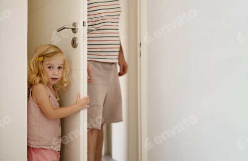Preview: Man and girl playing hide-and-seek at home.Child hiding behind door from parent, playing together