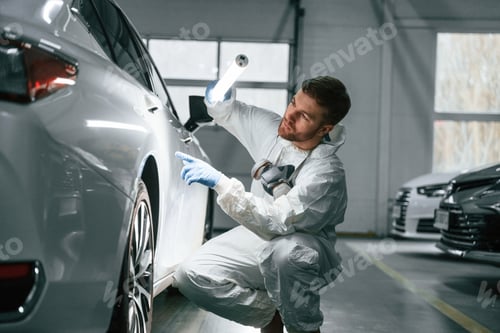 Preview: Searching for imperfections. Garage worker is holding lighting and checking surface of the car