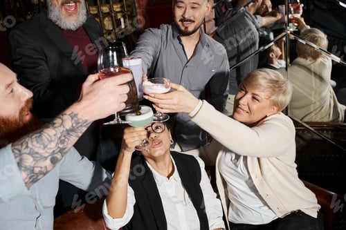 Preview: high angle view of multicultural workmates toasting with alcohol drinks in bar, after work fun