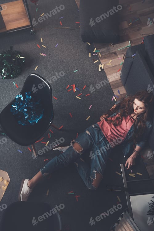 Preview: Top view of young drunk woman lying on floor in messy room