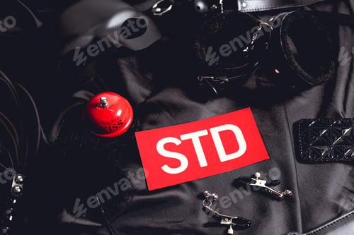 Preview: top view of red sex bell near paper with std lettering and sex toys on black