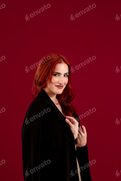 Preview: Confident woman looking at the camera while posing against a red isolated background.