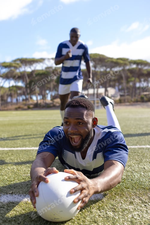 Preview: Two African American young male athletes are playing rugby on field outdoors, scoring a try