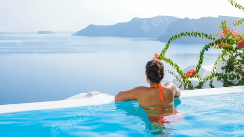 Preview: Young Asian women on vacation at Santorini relaxing in swimming pool looking out over Caldera ocean