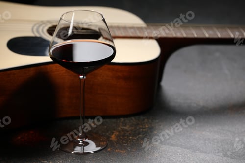 Preview: Acoustic guitar and red wine on black table, closeup