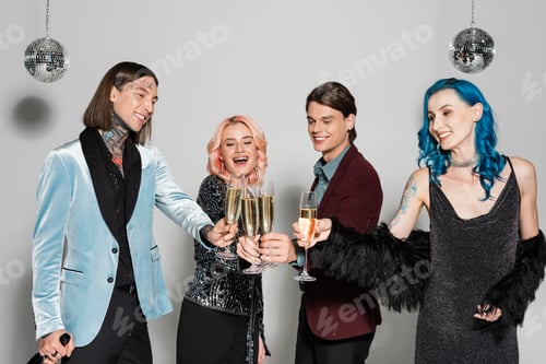 Preview: happy and stylish queer friends clinking champagne glasses during new year party on grey background